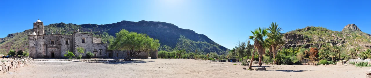 North side facade of Misión San Francisco Javier de Viggé-Biaundó. 
The mission appears on the left amongst its oasis surroundings of palm trees and mountain ranges. 270° Panorama.
Photo by Gregg M. Erickson.