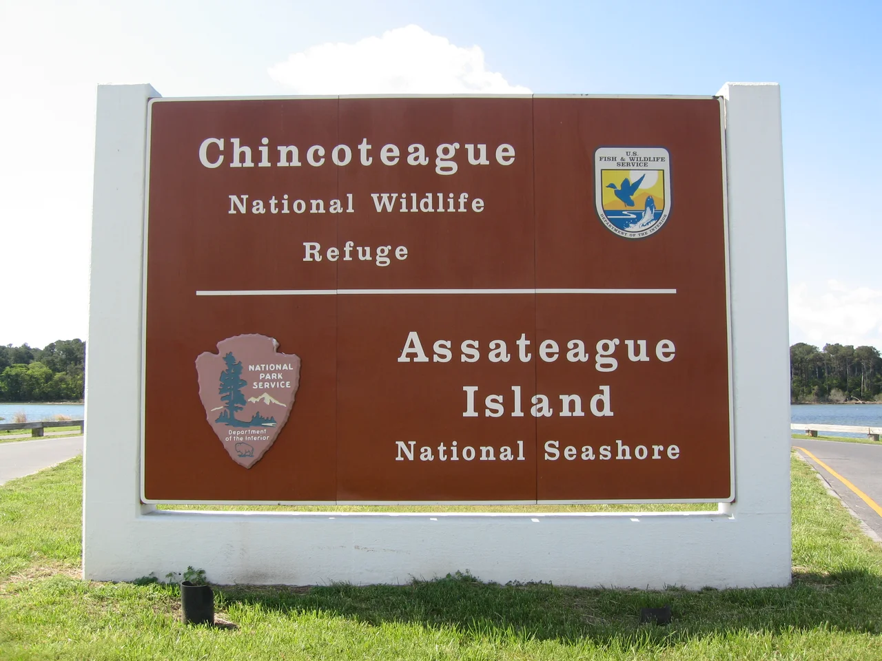 Chincoteague National Wildlife Refuge / Assateague Island National Seashore monument sign located at entrance to Assateague Island, Virginia. The Assateague Channel is in the background. Photograph taken in May 2008 from Maddox Boulevard facing southeast, showing the northwest face of the sign.