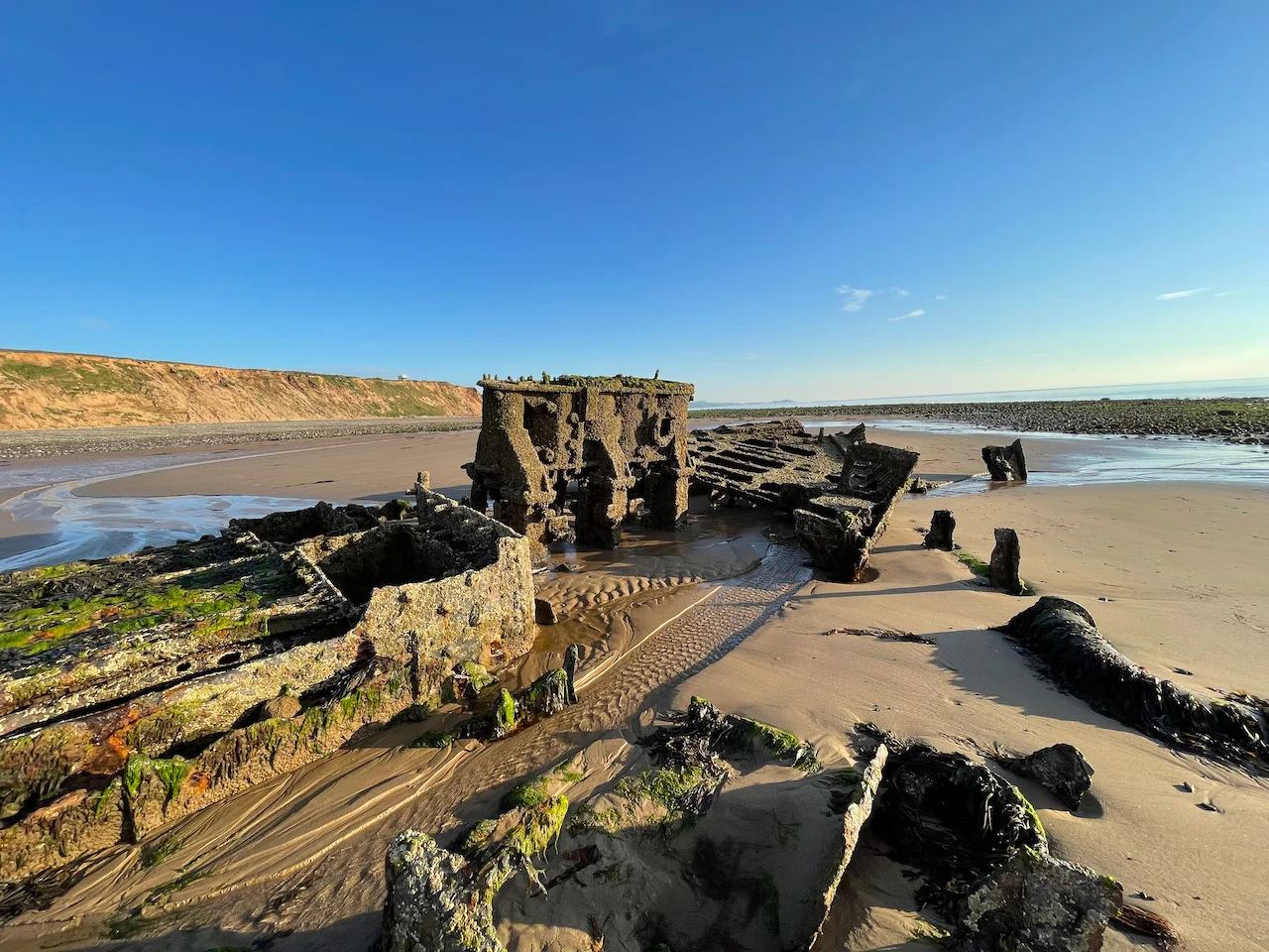 Close up view of stern section.  From left to right: boiler, engine, stern.  Background: cliffs of Jurby Head on the left, Peel Hill in the distance on the right.