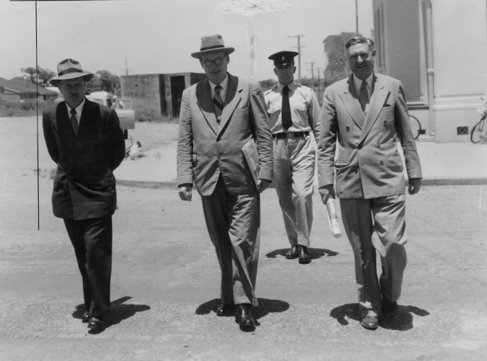 Members of the Collinsville Royal Commission, 1954
Members of the Royal Commission are being escorted by Constable Gordon Duncan at Bowen, during a break in proceedings. The members pictured are Walter Scott, Justice Sheehy (chairman) and Septimus Flowers. (Description supplied with photograph.).

The Royal Commission was being held into the cause of a 1954 poison gas explosion at Collinsville State Coal Mine which claimed seven lives.