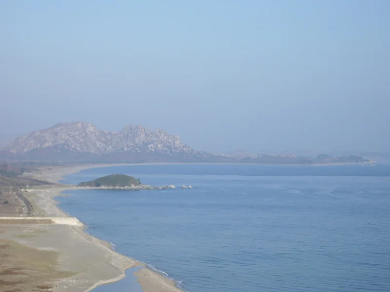 The turtle-shaped rock in the center left is the end of South Korean jurisdiction.
The peaks in the distance, and the peninsula jutting to the right, are North Korea.
The area in between is the Demilitarized Zone.
On the peninsula there is a small village visible. I was told that it was an empty propaganda village, just like dozens of others North Korea maintains along the border.
The beach looks lovely, and very inviting for a stroll. But it is safe to assume that landmines are everywhere down there, so even after permanent peace comes to the Korean peninsula, I can forget about a stroll down there.